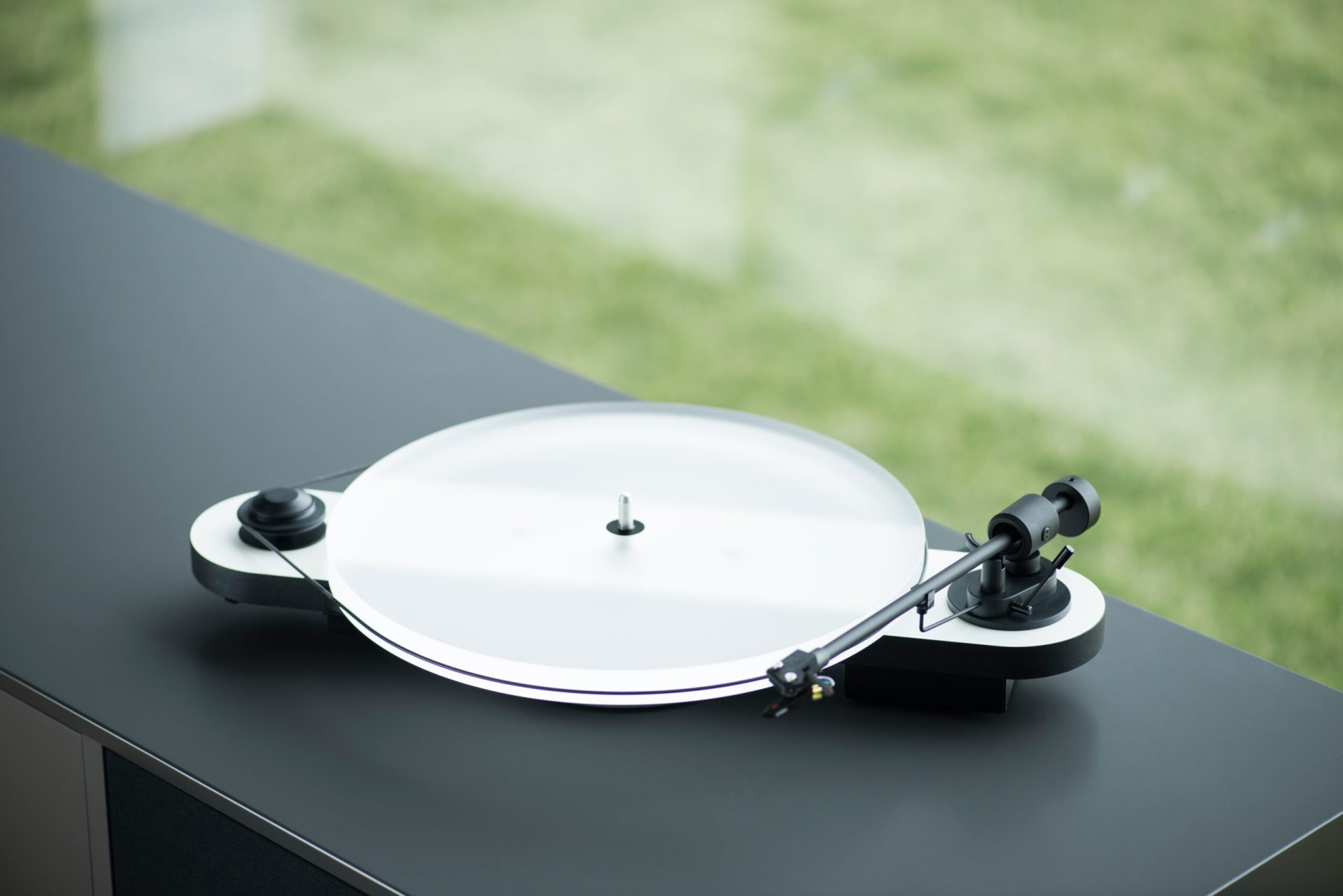 Por-Ject PJ Elemental in white with Acryl It E on top. The turntable is placed in a black furniture in front of a garden